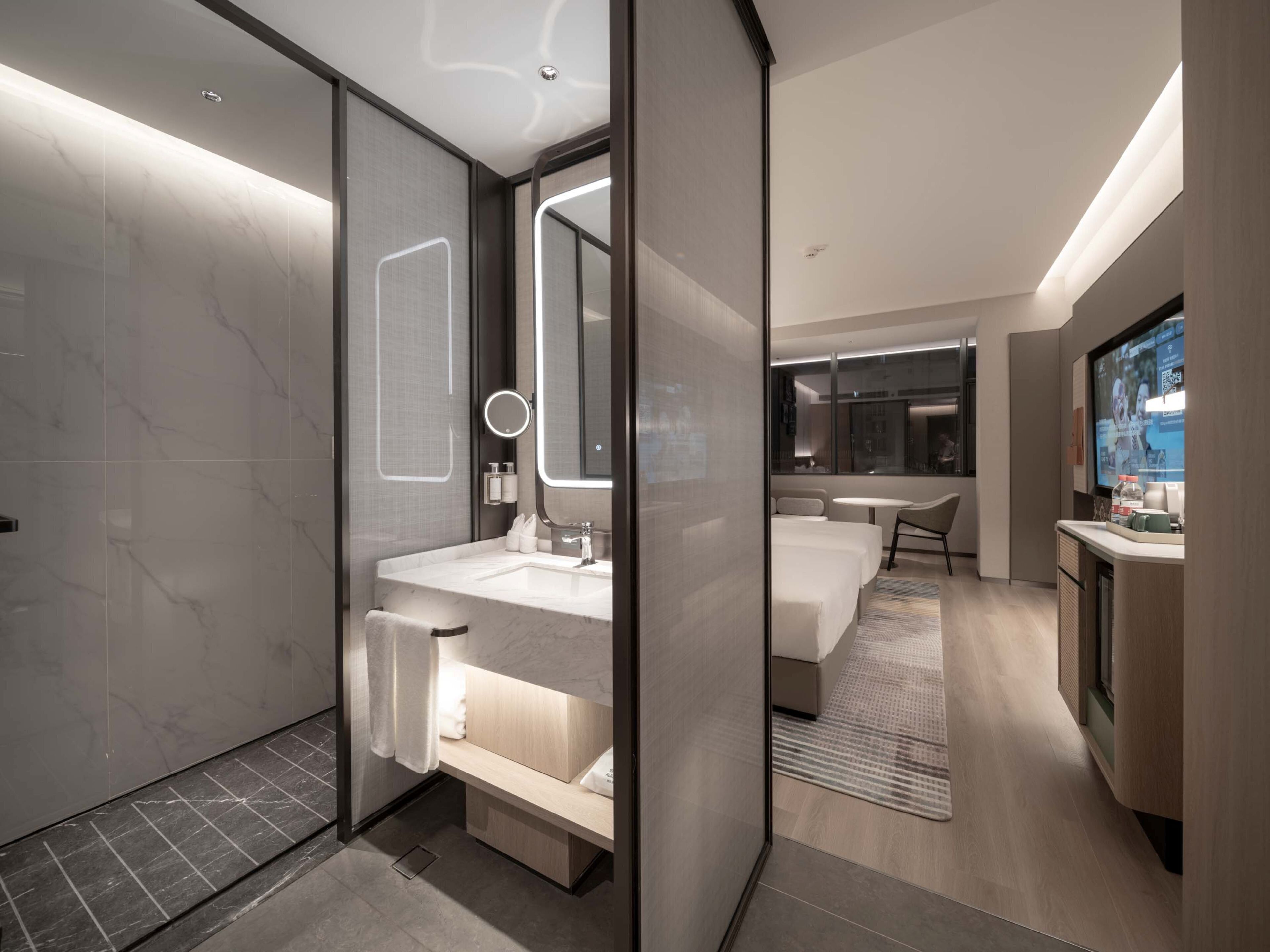 A modern hotel bathroom with a large mirror, a sink, and a shower area.