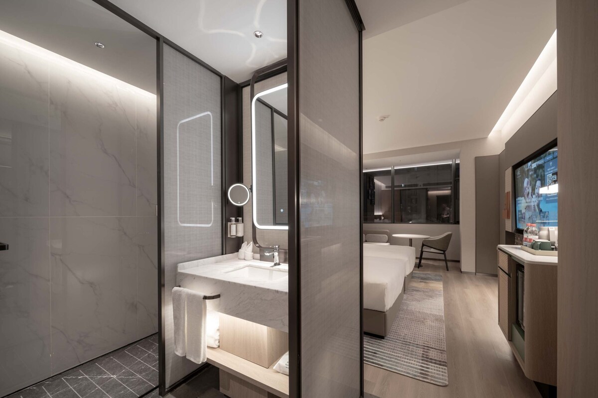 A modern hotel bathroom with a large mirror, a sink, and a shower area.