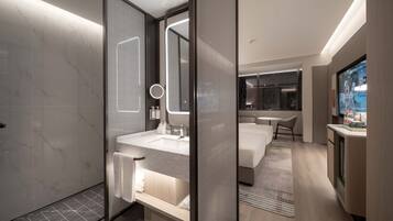 A modern hotel bathroom with a large mirror, a sink, and a shower area.