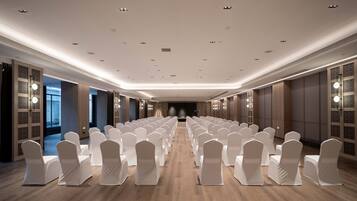 Un salón de conferencias con filas de sillas blancas, suelo de madera e iluminación empotrada.