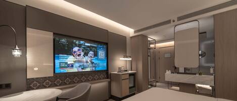 Una habitación de hotel moderna con cama, escritorio con silla, televisor montado en la pared y baño con espejo y lavamanos.