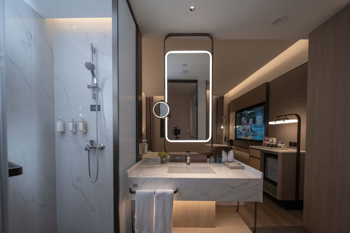 A modern bathroom with a shower, a vanity with a mirror, and a television screen.