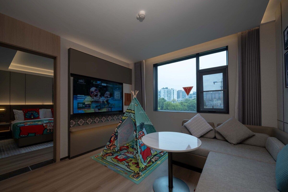A modern living room with a flat-screen TV, a sofa, a small round table, and a colorful children's play tent.