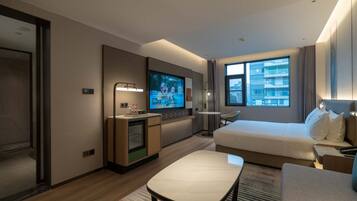 A hotel room with a bed, a desk, a TV, and a window with a city view.