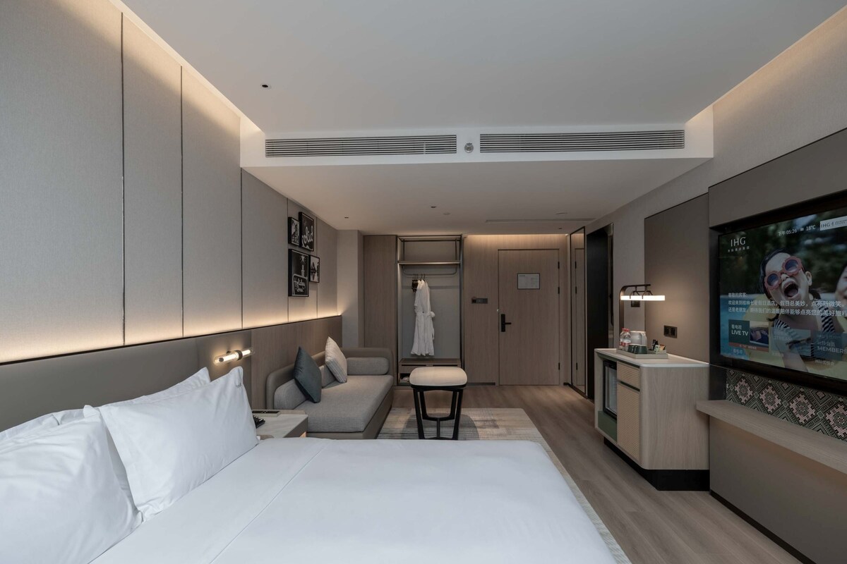 A modern hotel room with a large bed, a desk, a TV, and a wardrobe.