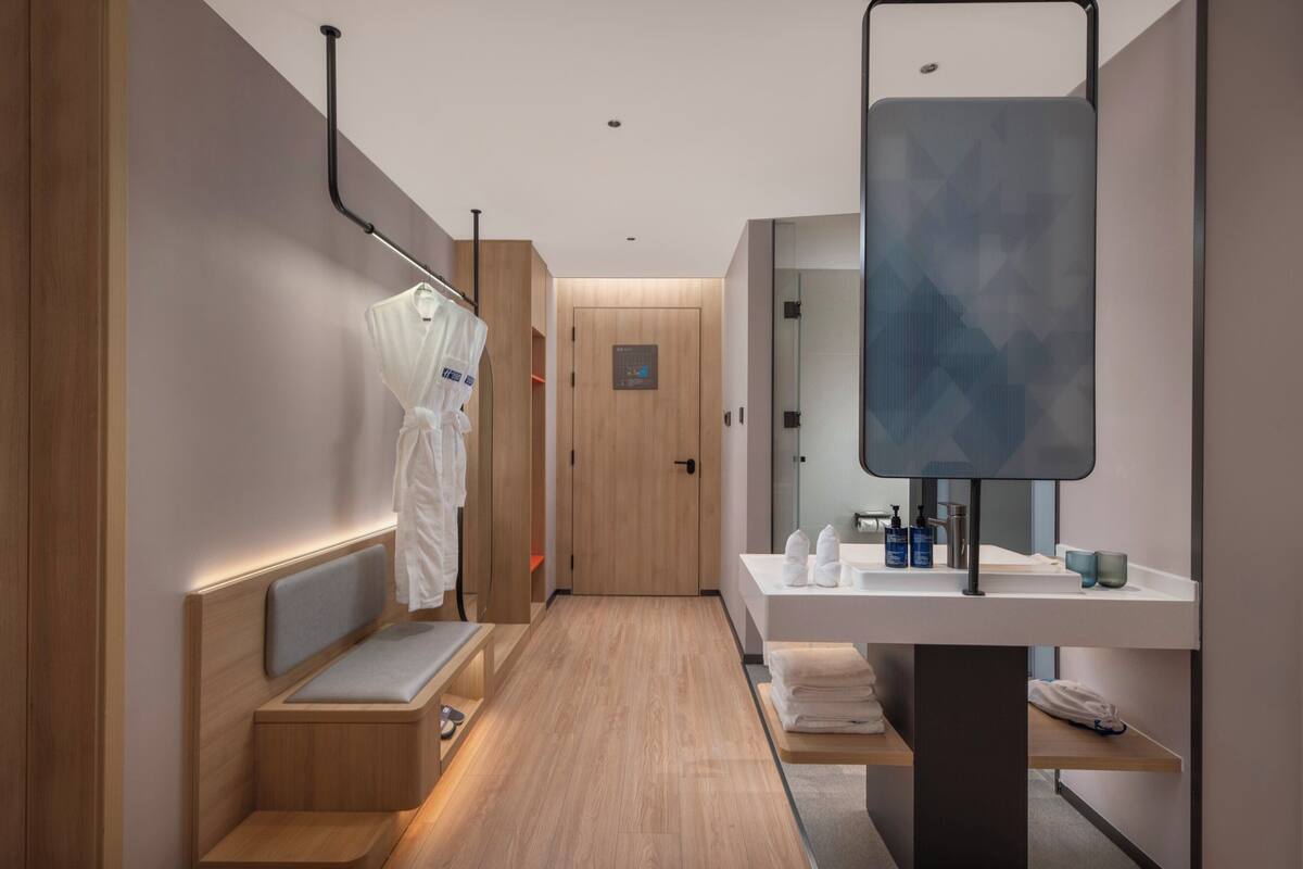 Une salle de bain moderne avec un banc en bois, un grand miroir et un lavabo agrémenté d’articles de toilette.