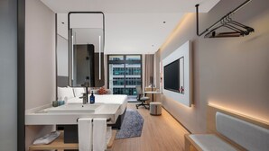 Een moderne hotelbadkamer met een grote spiegel, twee wasbakken, een bankje en een aan de muur bevestigde televisie.