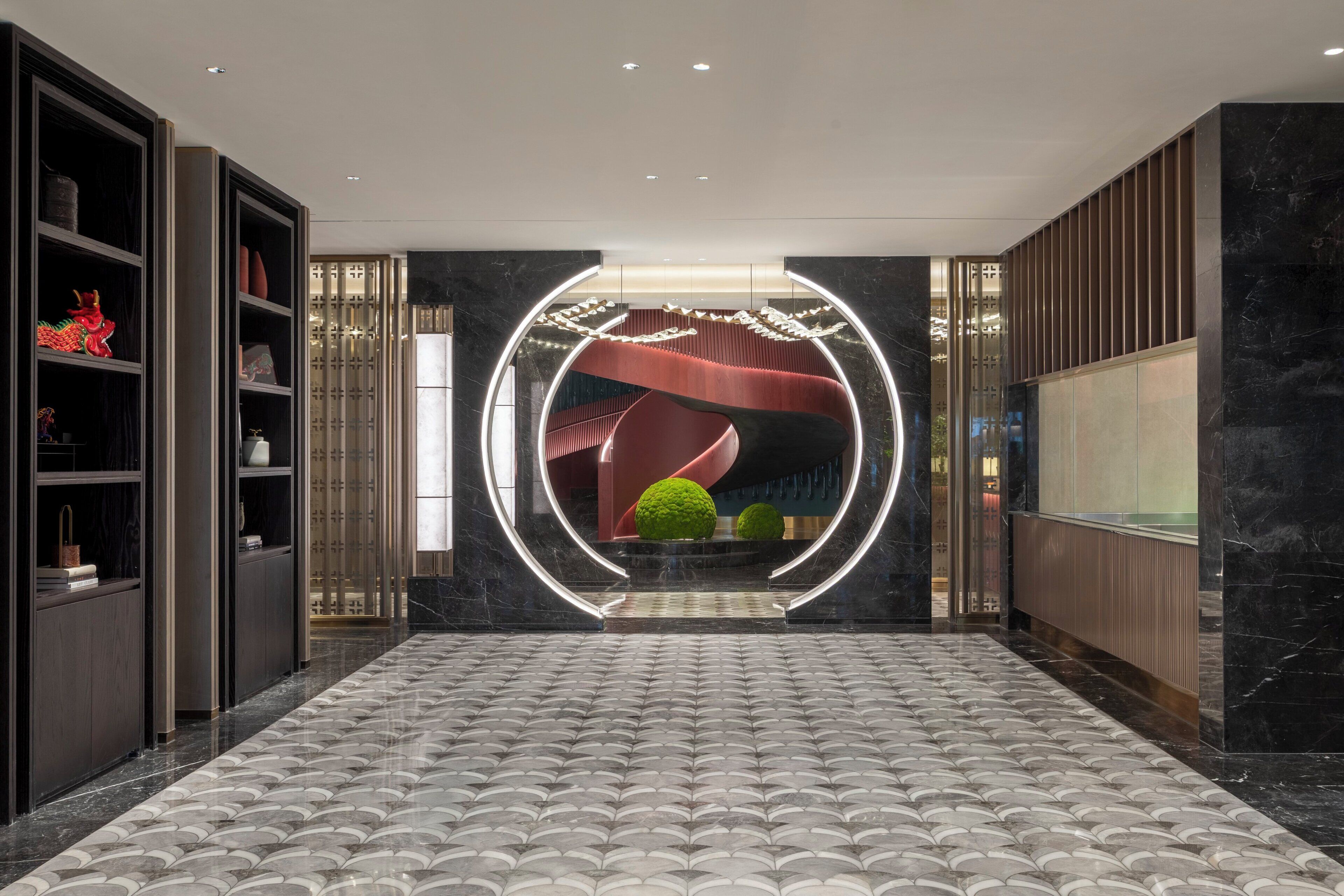 Un hall d’entrée moderne avec un sol à motifs, un luminaire circulaire central et un escalier menant aux étages supérieurs.