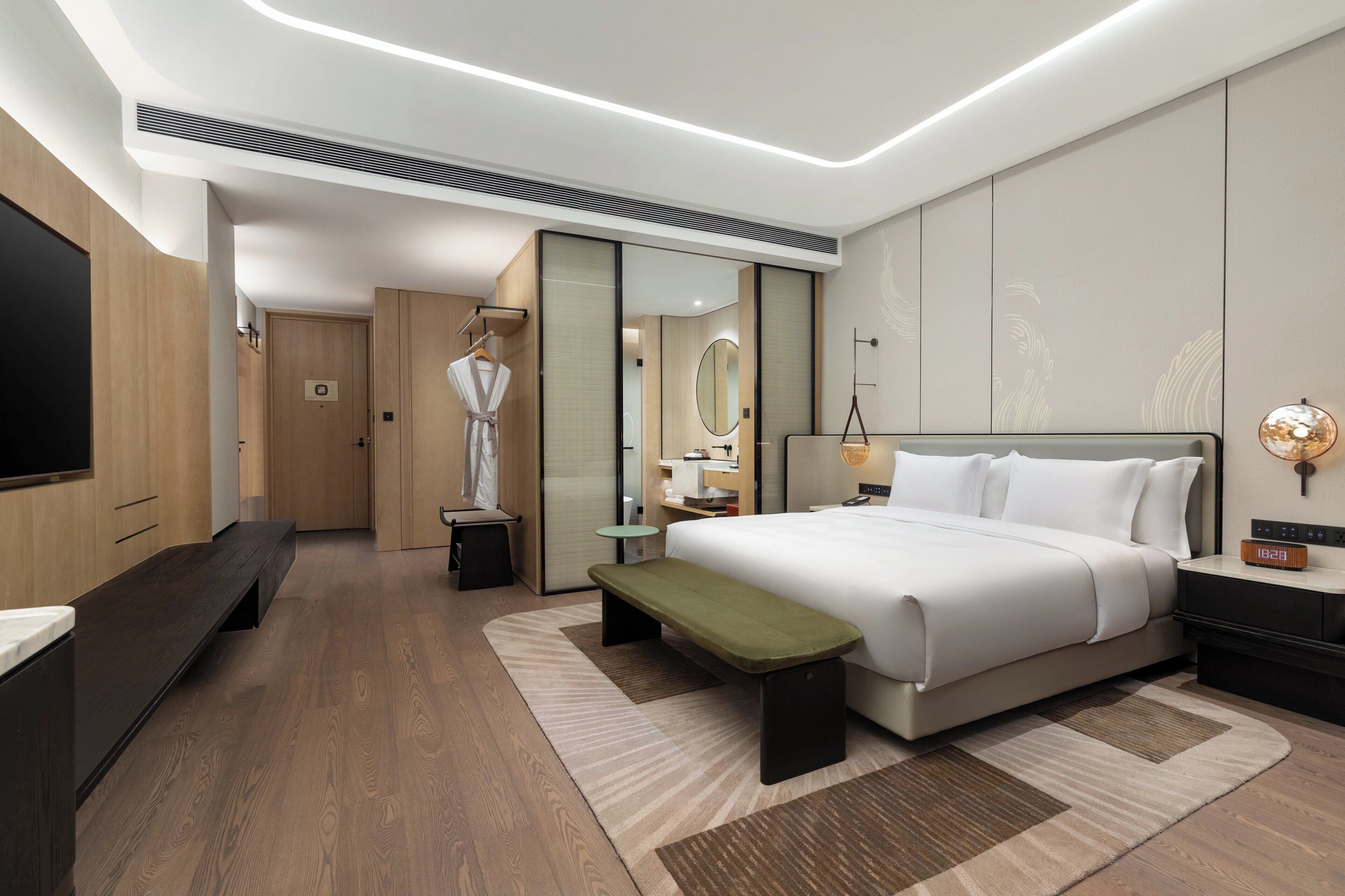 Et moderne hotelværelse med seng, bænk, natbord og et fjernsyn.
