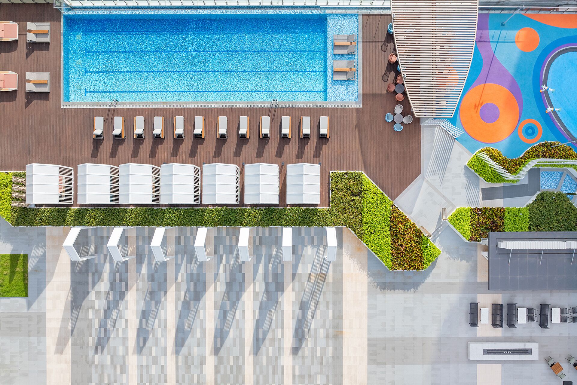 Une vue aérienne d’un hôtel avec une piscine, des chaises longues, des unités de climatisation et une fresque murale colorée.