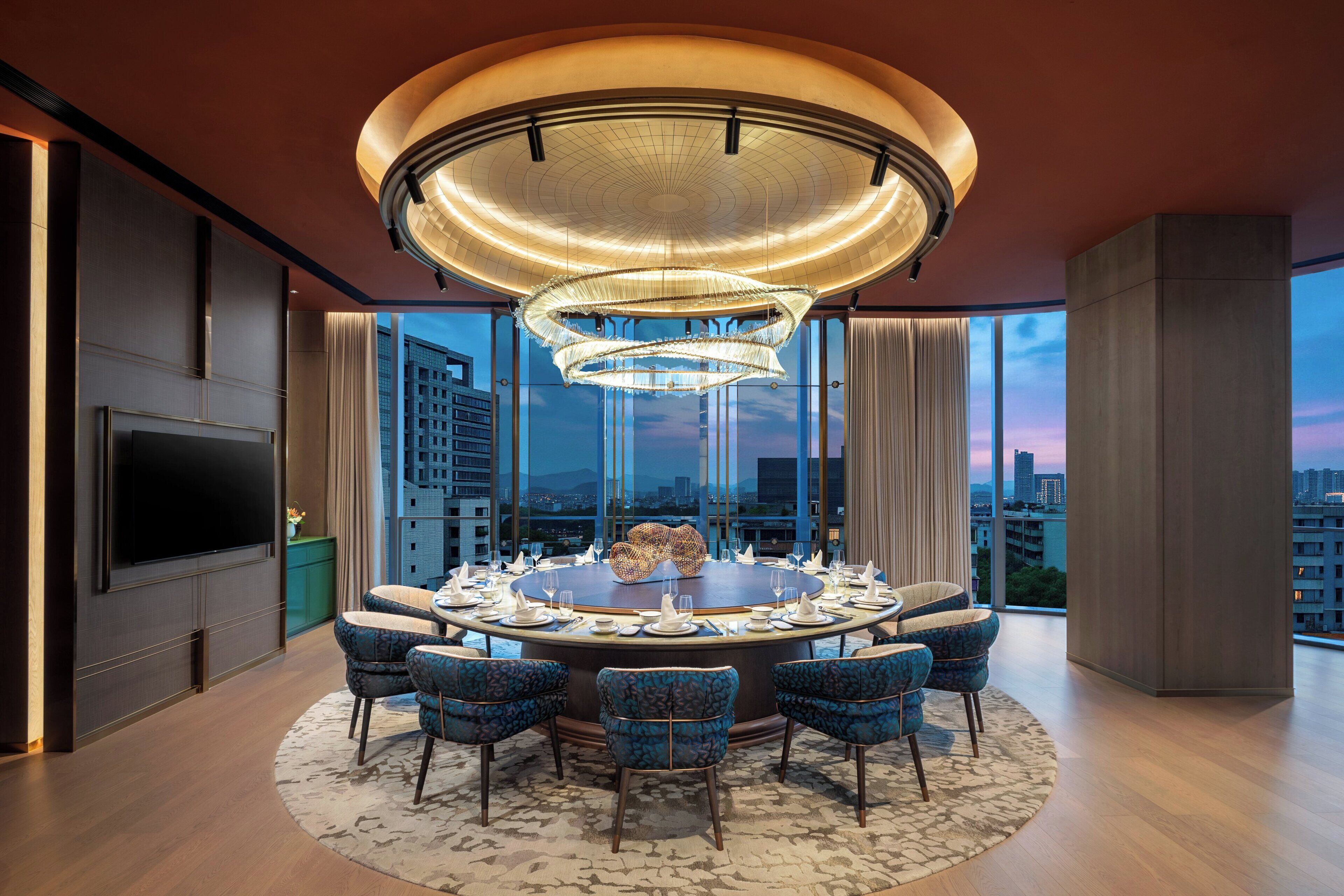 A modern dining area with a round table, chairs, and a large chandelier.