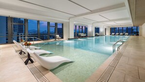 A large indoor swimming pool with clear water, modern lounge chairs, and a city view. - HUALUXE Zhongshan City Center (Zhongshan)