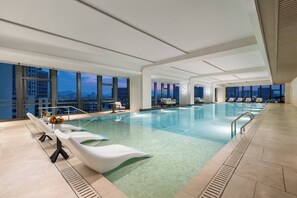 Ein großes Hallenbad mit klarem Wasser, modernen Liegestühlen und Blick auf die Stadt.