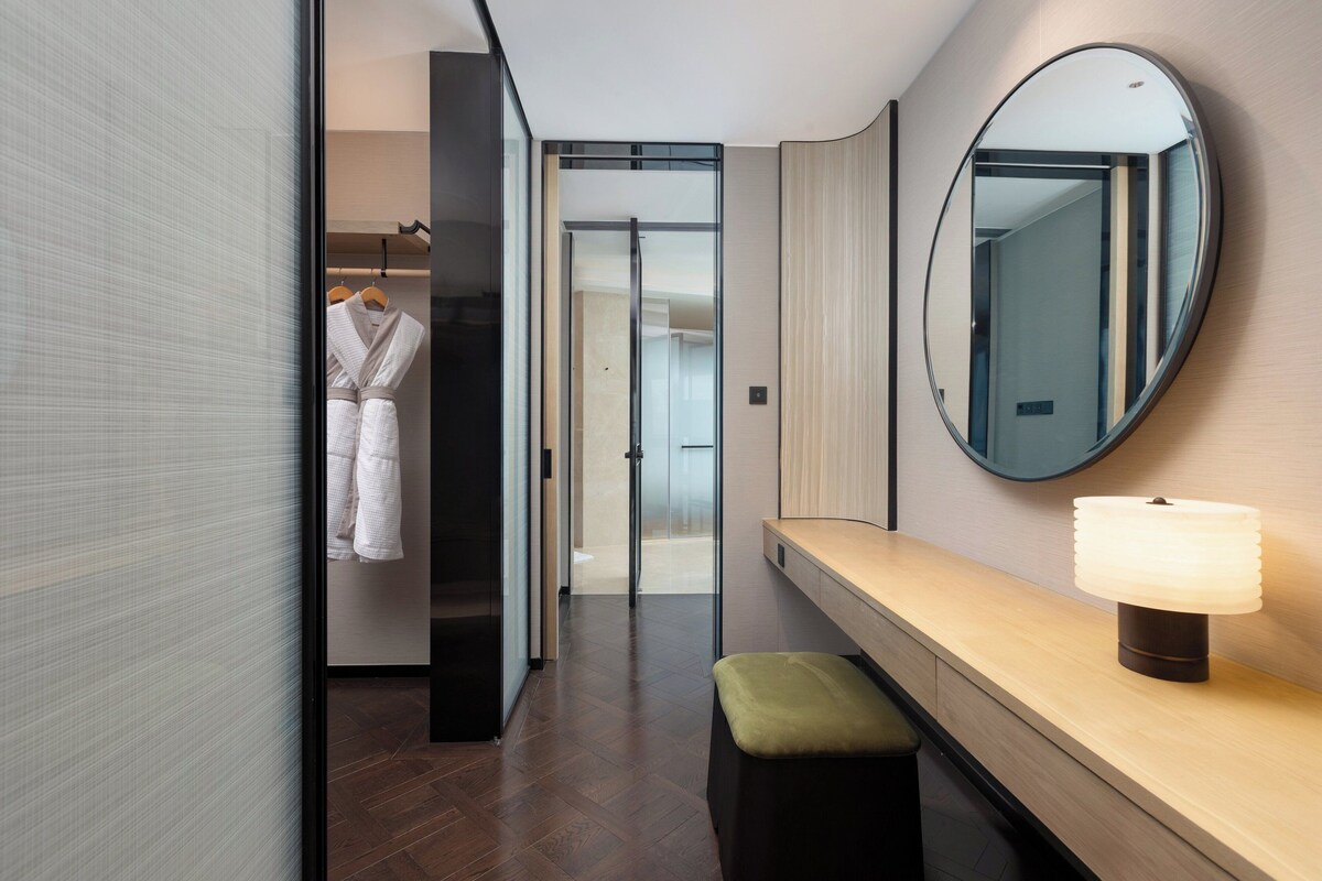 A modern bathroom with a large mirror, a bench, and a towel rack with robes.