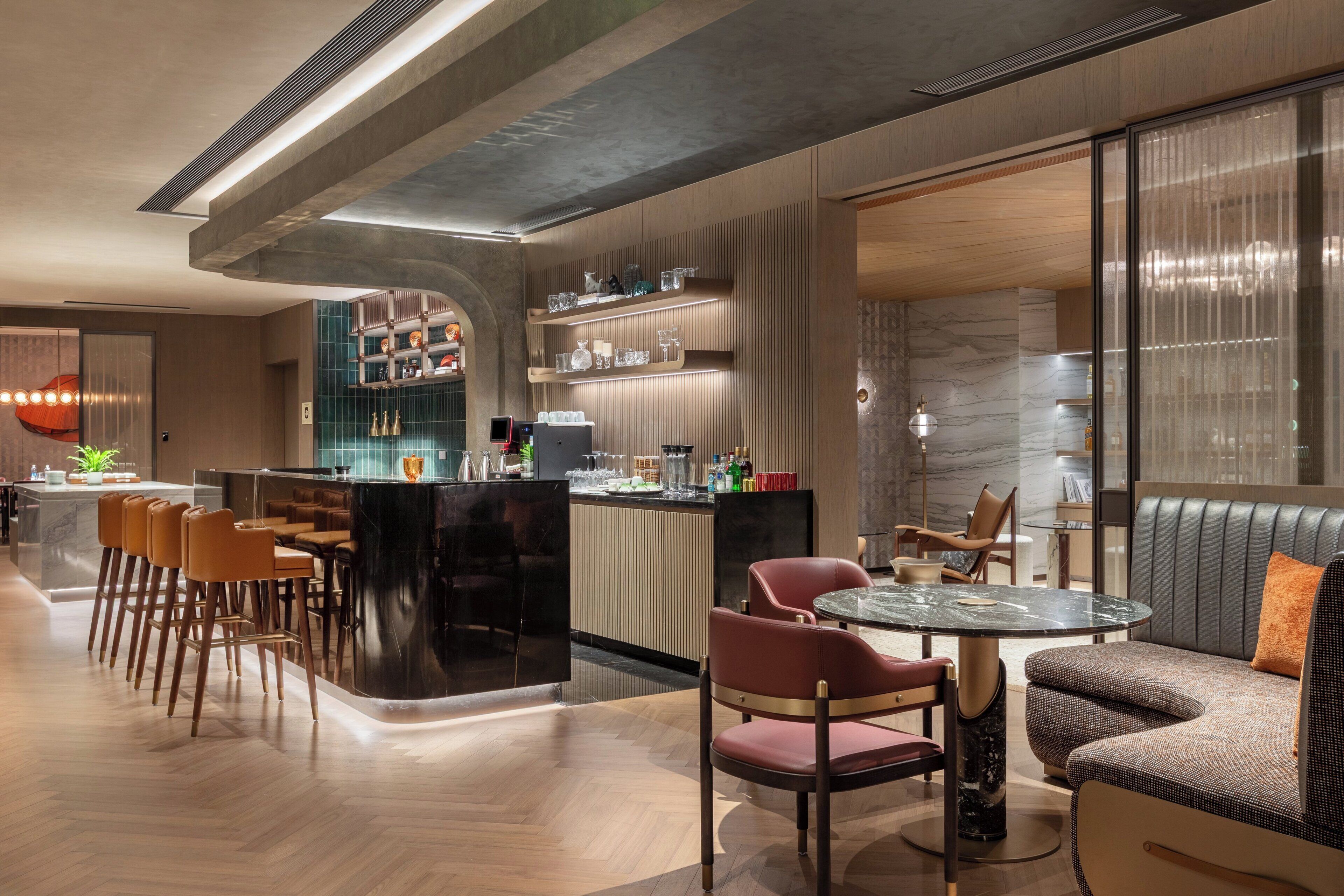 A modern bar area with a curved counter, seating with leather and fabric chairs, and a marble-topped table.