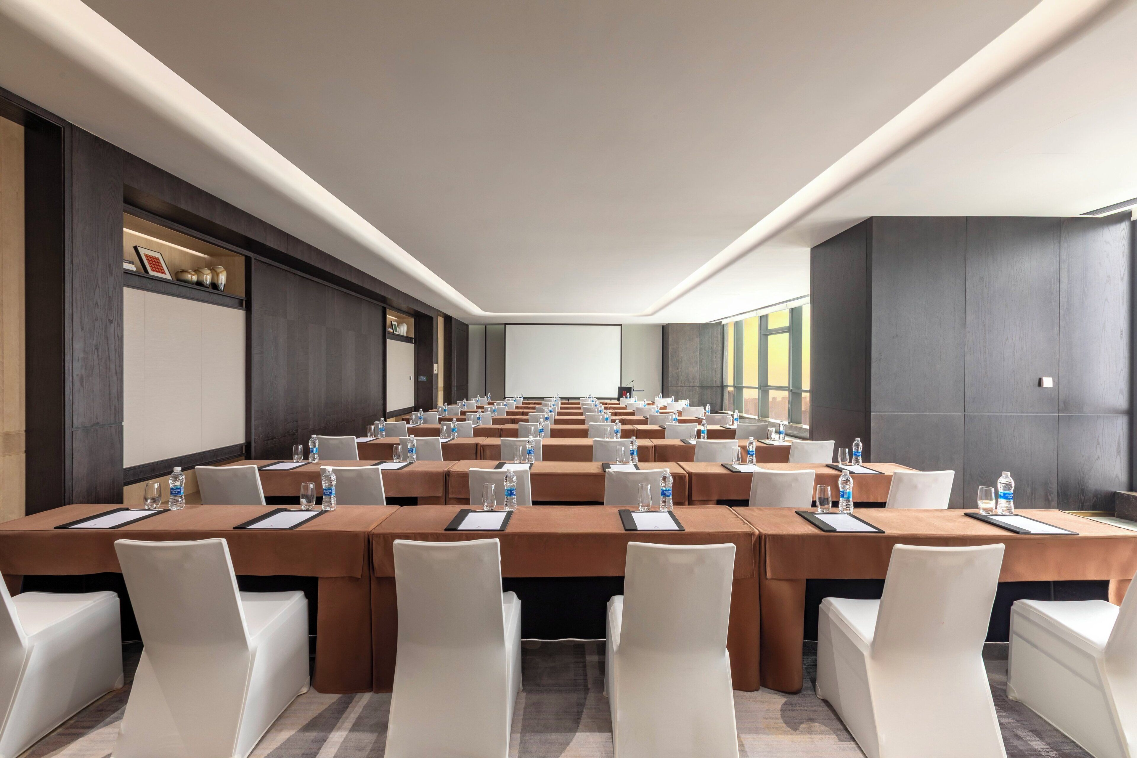A conference room with multiple tables, chairs, and a projector screen.