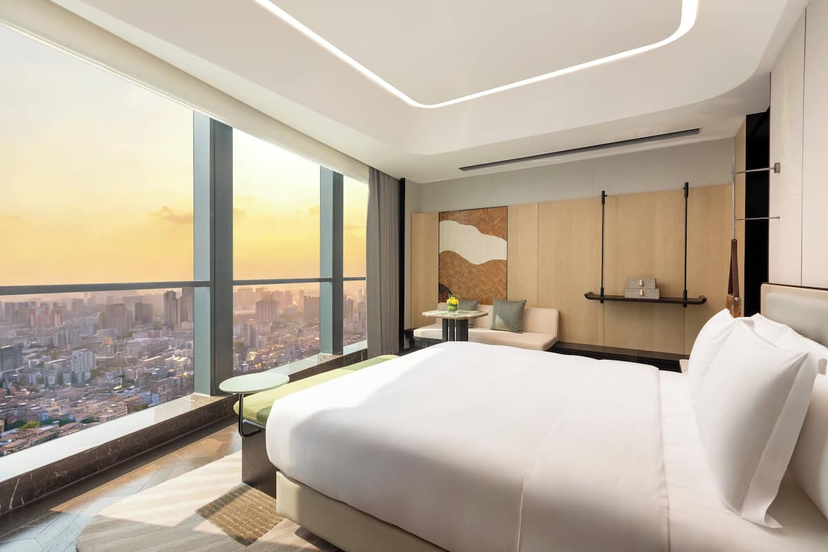 Ein modernes Hotelzimmer mit einem großen Bett, einer kleinen Sitzecke und Blick auf die Stadt.