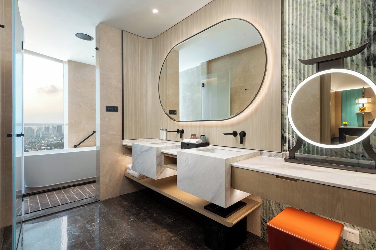 A modern bathroom with a large mirror, two sinks, and a view of the city.