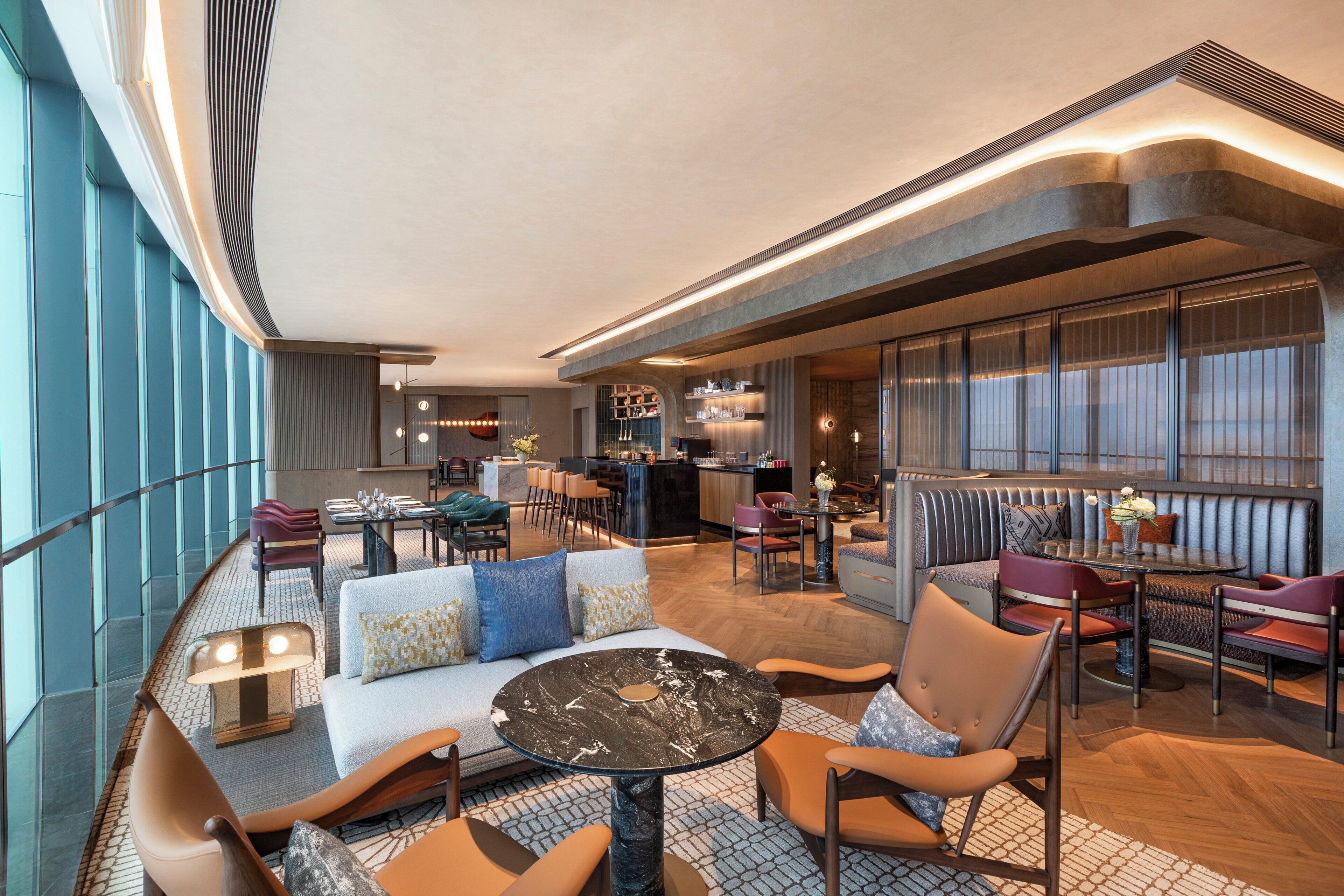 A modern hotel lobby with seating areas, a bar, and a kitchen in the background.