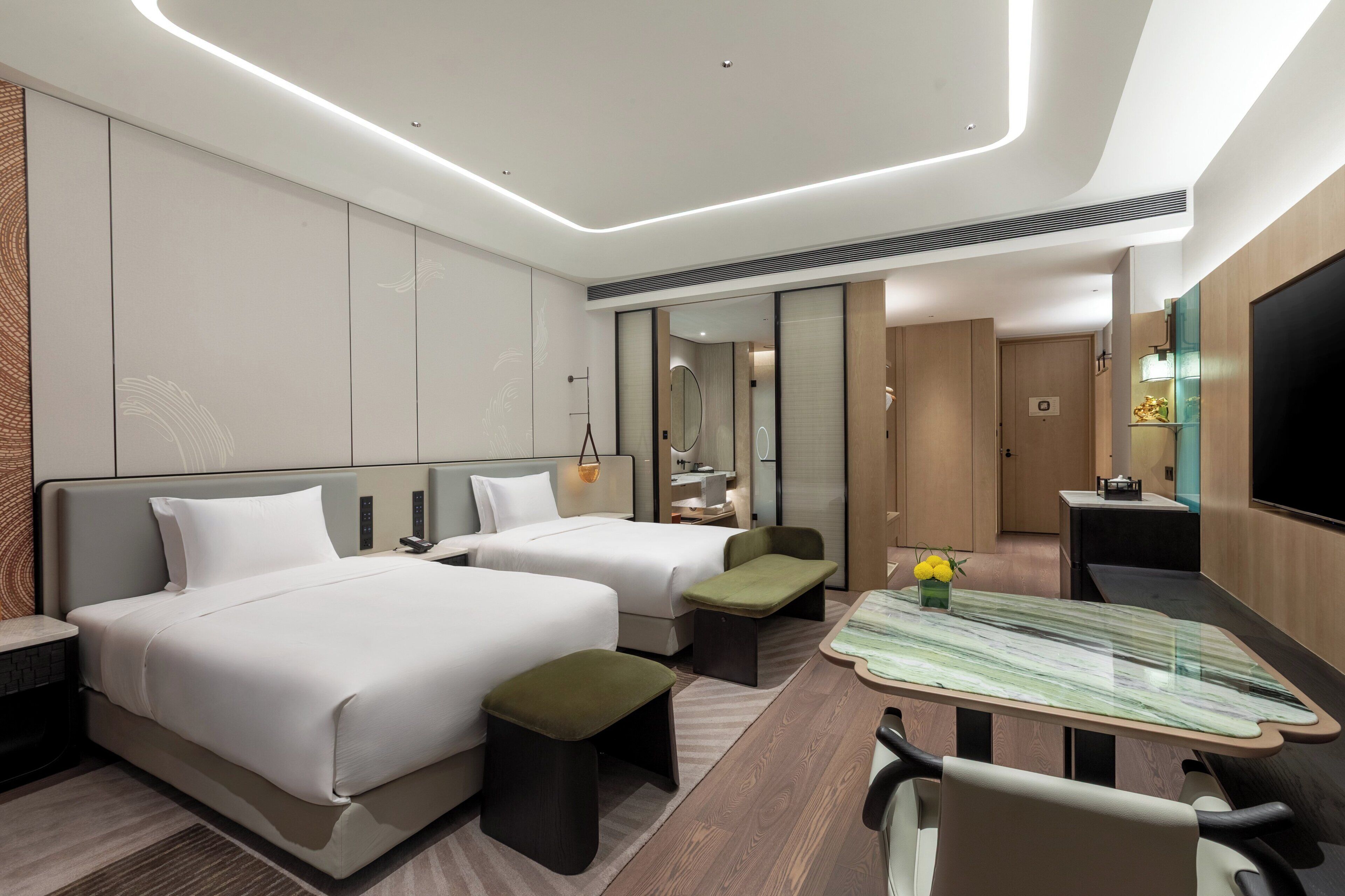 A modern hotel room with two beds, a desk, a mirror, and a TV.