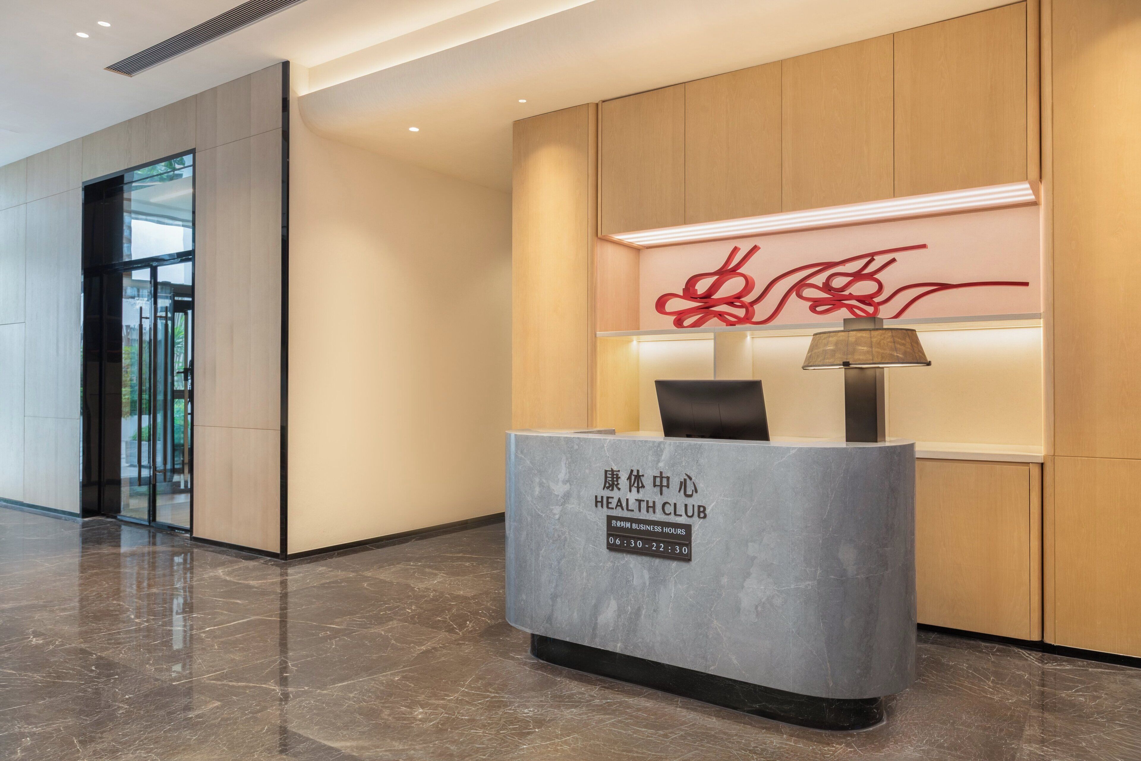 A reception desk with a sign indicating business hours, a modern interior with a marble floor, and a glass door entrance.