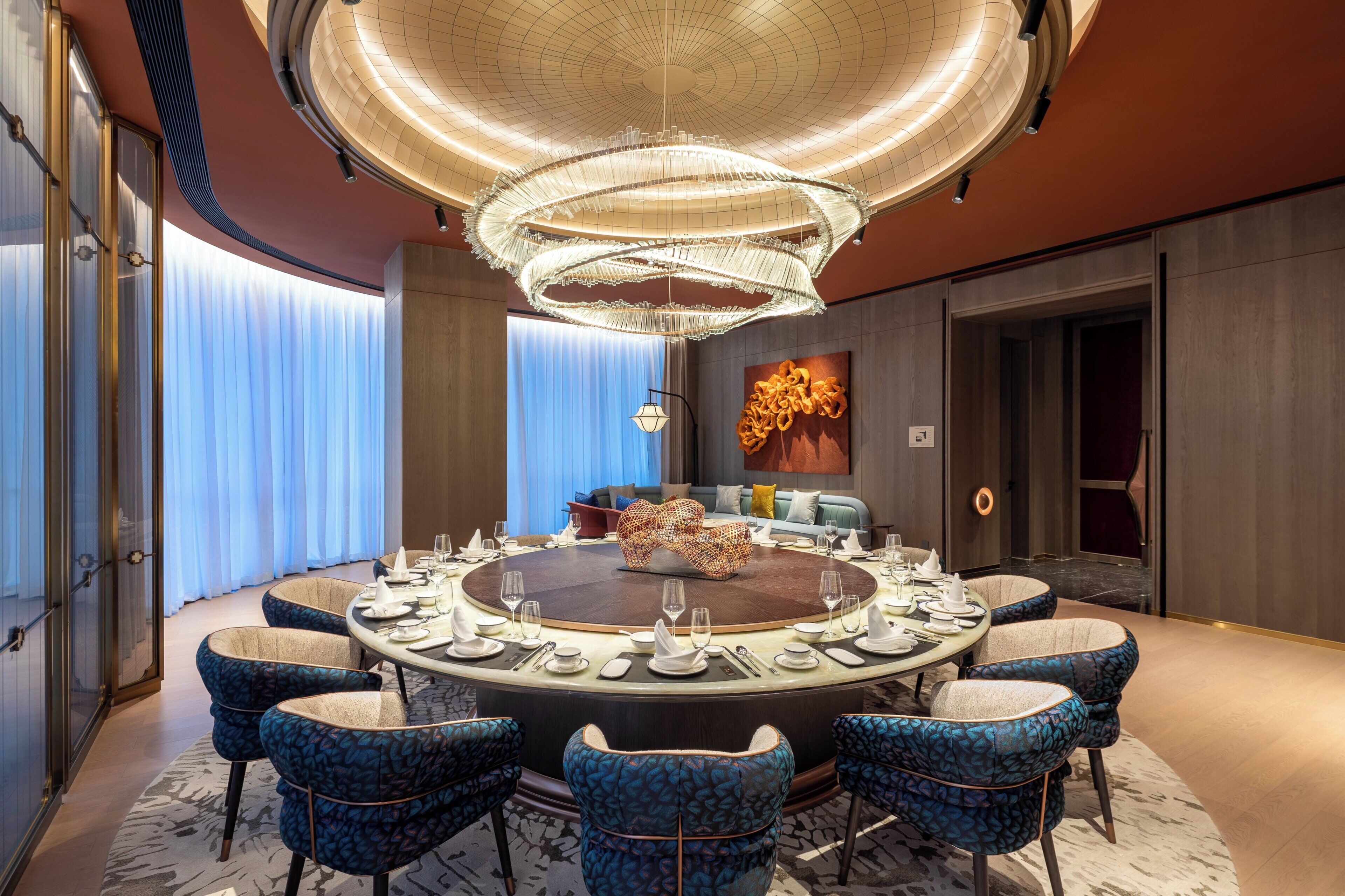 Una mesa de comedor redonda con sillas tapizadas en azul, una araña y una decoración de interiores moderna.