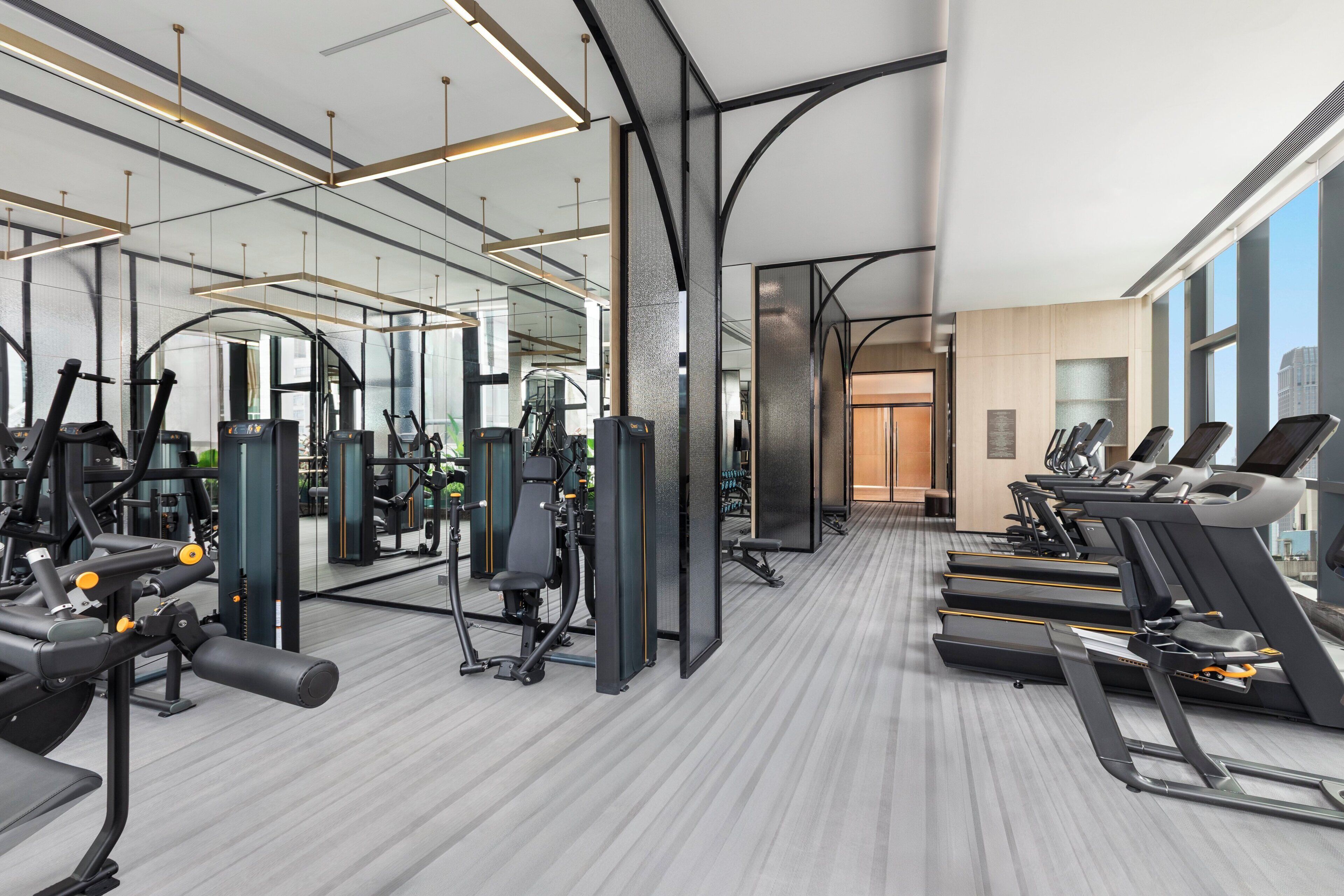 A modern gym with treadmills, weight machines, and a mirrored wall.
