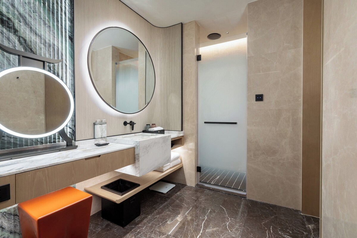 A modern bathroom with a vanity, a large mirror, a shower, and a bench.