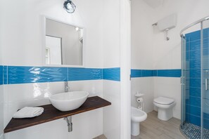 Une salle de bain avec un lavabo blanc, un miroir, des toilettes et une douche.