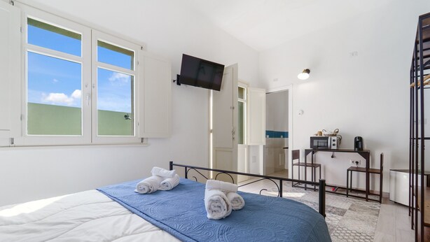 Une chambre à coucher avec un lit, un téléviseur fixé au mur et un bureau avec une chaise.