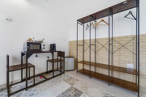 A room with a kitchenette, a wooden bench, a hanging clothes rack, and a brick-patterned wall. - Room 6 – Double Room with Garden View (Assemini)