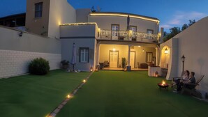 Une maison à deux étages avec un balcon, une pelouse bien entretenue et un espace extérieur aménagé pour s’asseoir.