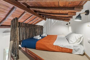Een bed met een houten hoofdbord, een blauw-oranje dekbedovertrek, witte kussens en een hangende lamp.