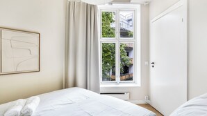 Ett sovrum med ett stort fönster, en säng, ett element och en dörr.
