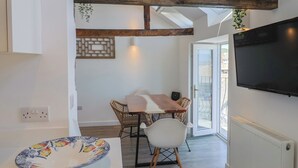 Una cocina moderna con techo de vigas de madera, un área de comedor con sillas de mimbre, un televisor grande y vistas a través de un ventanal.