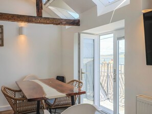 Una stanza con un tavolo in legno, sedie in vimini, una porta in vetro che dà su un balcone con vista sul mare.