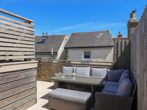 Une terrasse avec une table et des chaises, une clôture en bois et, au fond, un bâtiment doté d’un toit en pente.