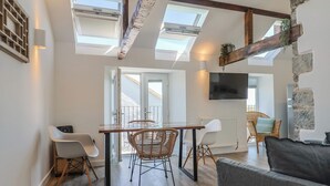 Una sala de estar moderna con comedor, vigas de madera, tragaluces, un televisor de pantalla plana y una pared de acento de piedra.