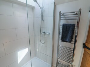 A shower with a glass enclosure, a towel rack, and a tiled floor. - Avocet (Lyme Regis)