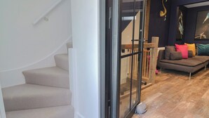 Una sala de estar moderna con un sofá, una escalera y un vidrio que da a otra habitación.