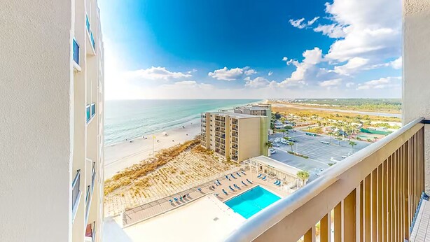 A balcony with a view of a beach, a pool, and a parking area. - Pinnacle Port A-929 (Panama City Beach)
