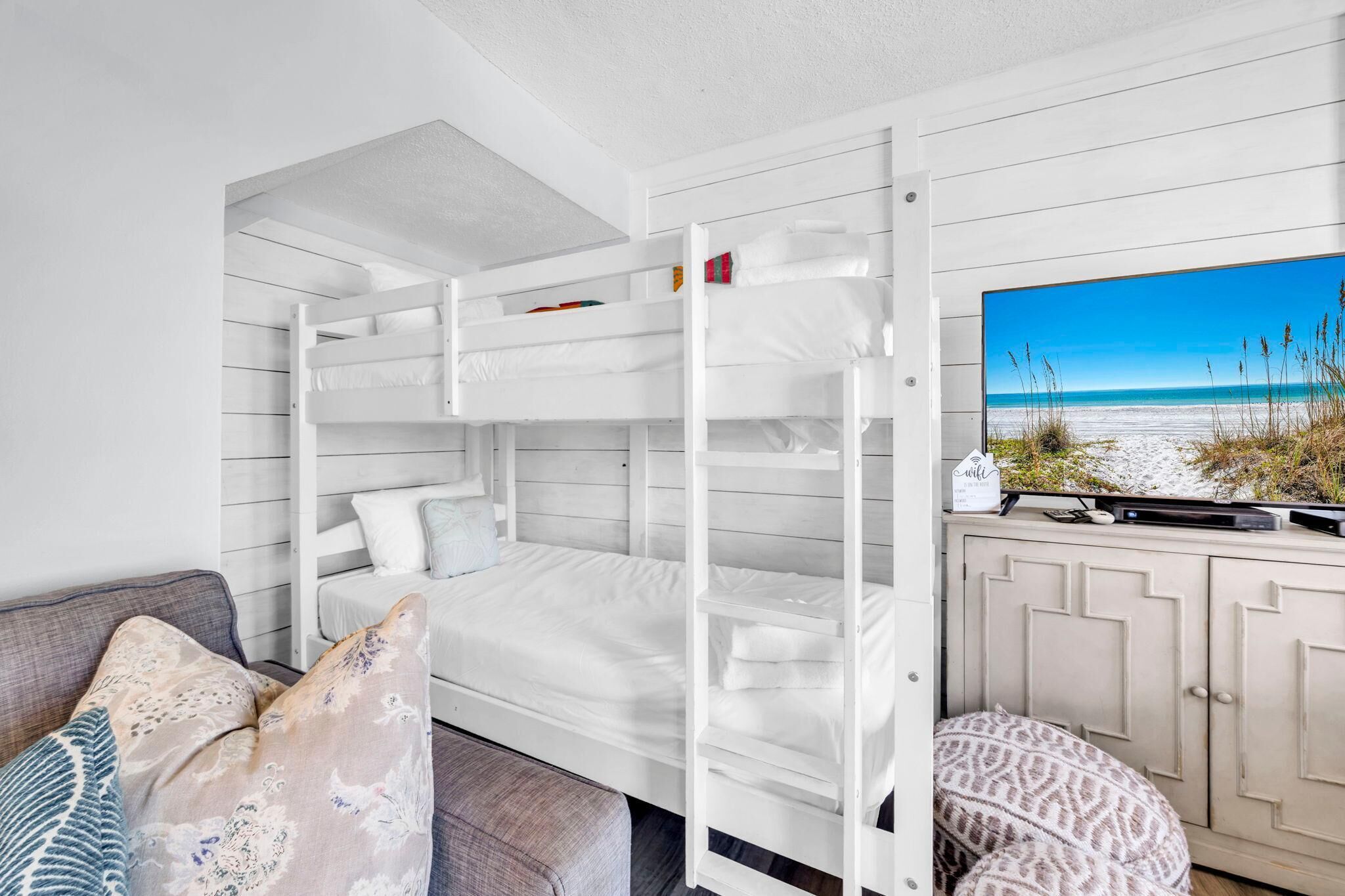 A bunk bed room with a view of the beach, a sofa, and a cabinet.