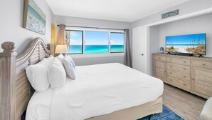 A bedroom with a large bed, a dresser, and a painting of a beach. - Pinnacle Port A-929 (Panama City Beach)