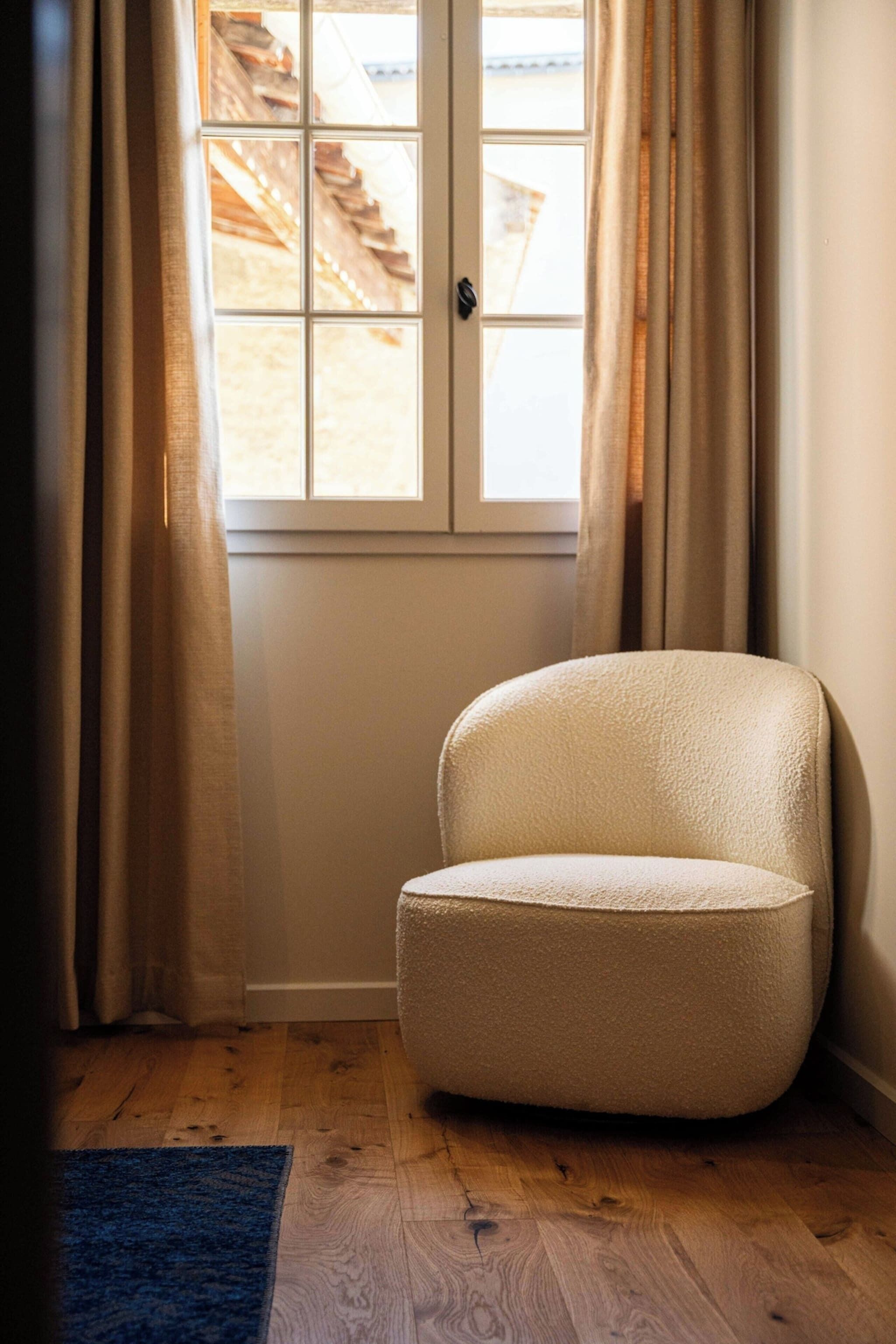 A corner room with a window, a chair, and wooden flooring.