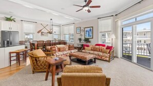 A spacious living room with a sectional sofa, a dining area with chairs, a kitchen with cabinets, and a balcony with a view. - Gorgeous Beach Retreat Semi-Private Pool Views Bikes Grill (Ocean City)