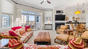 A spacious living room with a sofa, ottoman, and wicker chairs, a ceiling fan, and a view through large windows. - Gorgeous Beach Retreat Semi-Private Pool Views Bikes Grill (Ocean City)