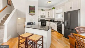 A modern kitchen with white cabinets, a black refrigerator, and a wooden island with stools. - Gorgeous Beach Retreat Semi-Private Pool Views Bikes Grill (Ocean City)
