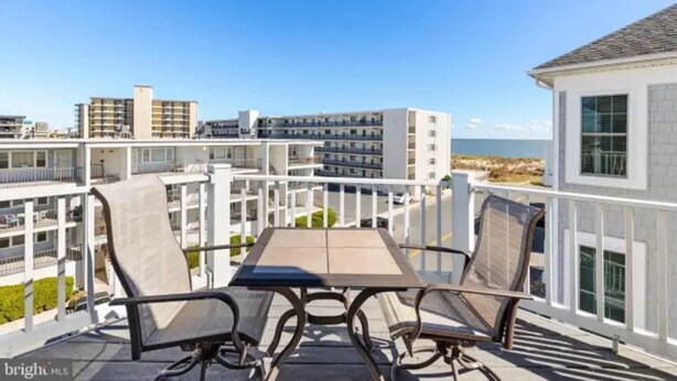 A balcony with a table and chairs, overlooking a beach and buildings. - Gorgeous Beach Retreat Semi-Private Pool Views Bikes Grill (Ocean City)