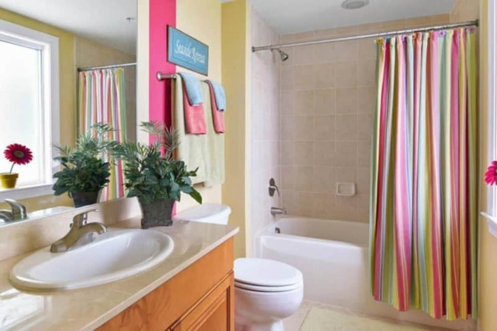 Un baño con bañera, ducha, inodoro y lavabo. Hay toallas colgadas en la pared y un cartel sobre la bañera.