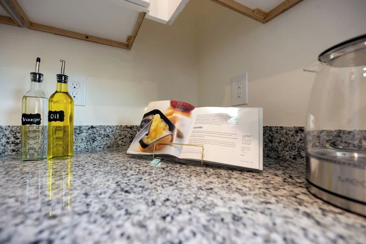 Eine Küchenarbeitsplatte mit zwei Flaschen, beschriftet mit 'Vinegar' und 'Oil', einem offenen Kochbuch und einem Edelstahlkochtopf.